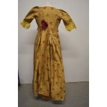 A 19th century gold dress with embroidered floral sprigs, having open skirt, train to back, hook and