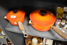 Two modern Le Creuset lidded sauce pans in orange enamel.