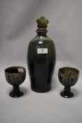A Woburn studio pottery decanter and two goblets, having green and brown mottled glaze.
