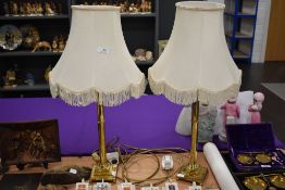 A pair of traditional brass table lamps with cream shades.