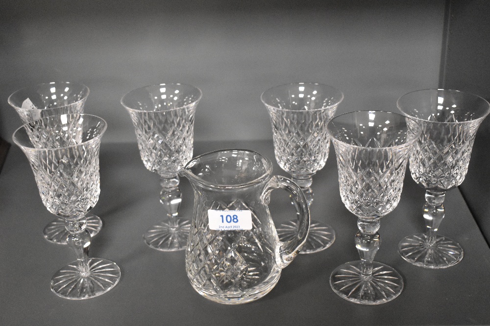 A set of six modern clear cut crystal wine glasses and a water jug.