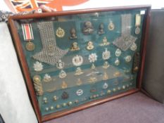 A wooden and glazed display containing approx 60 Military Items including Medals, Cap Badges,