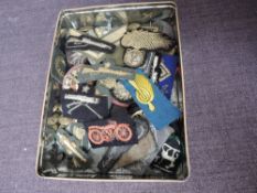 A tin containing Military Cloth Badges and Pips, Brass Buttons, Metal Cap Badges and a MK 384