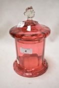 A Victorian cranberry glass sweet jar with a clear glass handle, small chips to rim and lid.