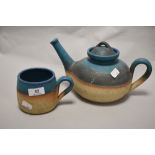A studio pottery teapot and mug, having teal blue banded glaze to natural ground.