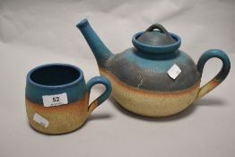 A studio pottery teapot and mug, having teal blue banded glaze to natural ground.