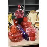 A collection of vintage cranberry glass wares including water jugs, vases and bowls.