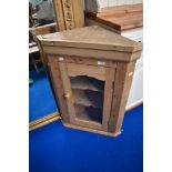 A stripped pine corner wall cupboard having glazed door