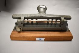 A large vintage desk top hole punch, mounted on wood block.