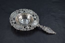 A Dutch white metal straining spoon, the dished and pierced central well within a pierced C-scroll