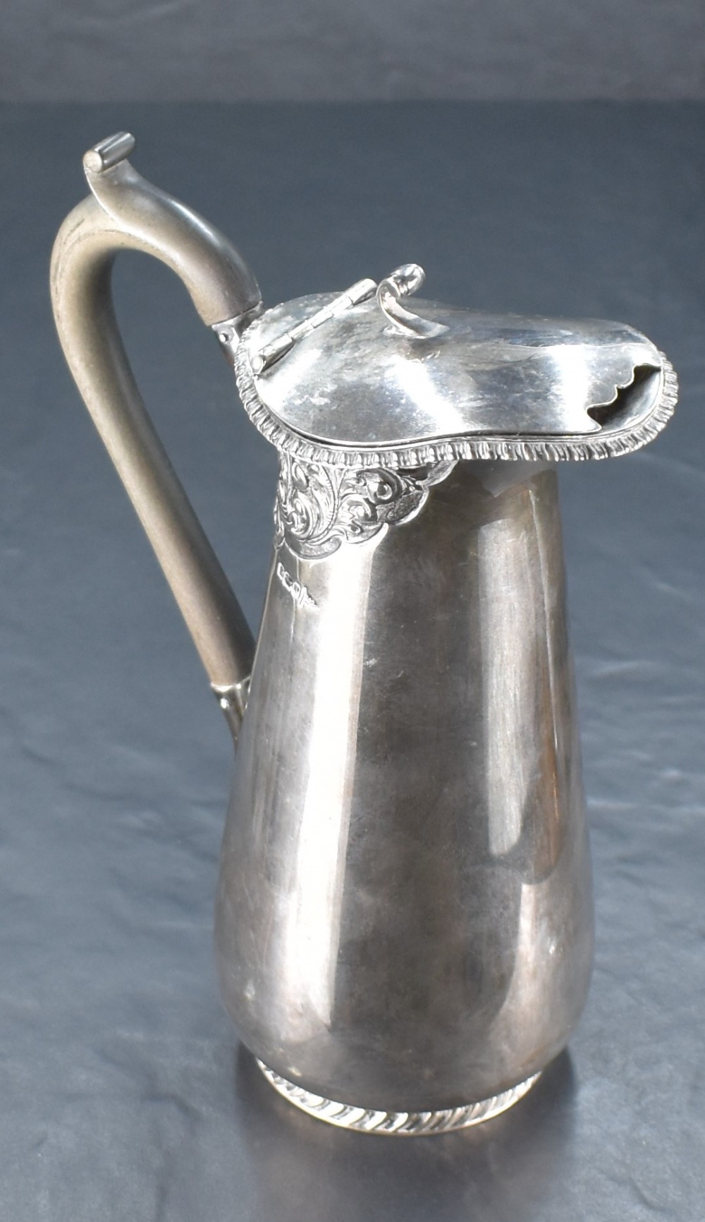 An Edwardian silver water jug, having a hinged cover with scrolled thumb piece over the gadrooned