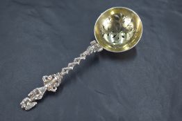 An ornate Victorian silver sifting spoon, the pierced circular bowl issuing an ornate cast figural