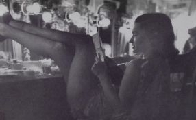 A reproduction monochrome photographic print, a 1950's showgirl relaxing between performances,