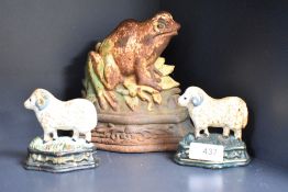 A cast iron door stop in the form of a frog and two smaller examples in the form of sheep.