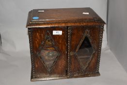 An early 20th century oak smokers cabinet, having two doors with diamond shaped glass and beaded