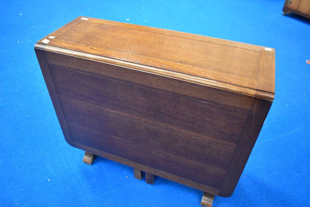 A 20th century oak drop leaf space saving table, with gated supports, end drawer and cupboard