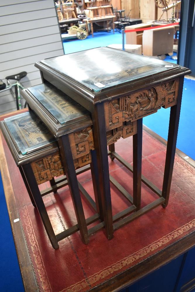 An Oriental nest of three tables with carvings to frieze and under glass to top