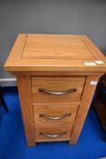 A modern golden oak three drawer bedside chest