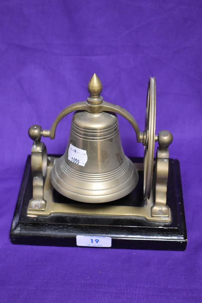 A solid brass and mounted table top ship's bell raised on a stepped rectangular plinth, 18cm tall