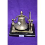 A solid brass and mounted table top ship's bell raised on a stepped rectangular plinth, 18cm tall