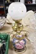 A brass table lamp in the form of an oil lamp and ceramic lamp base with floral decoration.