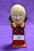 An early 20th Century novelty cast iron money bank in the form of Humpty Dumpty sitting on a red