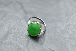 A jade style oval cabochon ring in a claw set mount on a white metal loop stamped 18ct, size L &