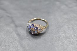 A tanzanite and diamond daisy cluster ring having a diamond chip oval border on a 14ct gold loop,