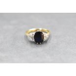 A sapphire ring having a central facet cut oval stone having a trio of small diamonds to each side