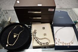 A modern three-drawer jewellery case containing a variety of white metal and costume earrings,