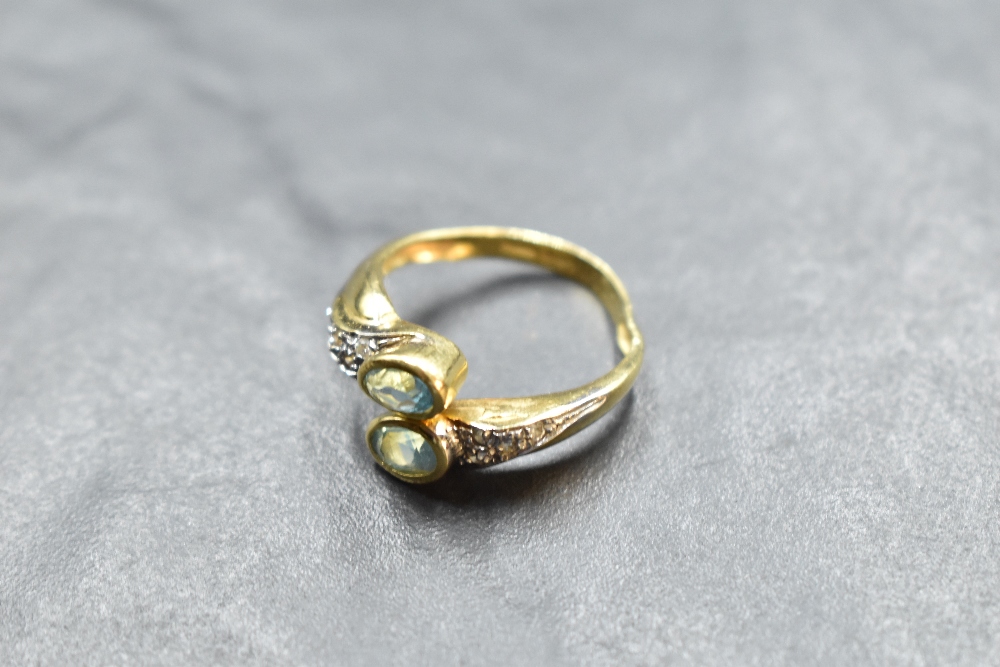 An 18ct gold open crossover ring having oval blue topaz to terminals and white stones to