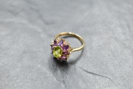 A large amethyst and diamond chip oval cluster ring with central green gem in a stepped claw set