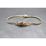 A 9ct gold bracelet having a central panel with three rubies in an open swirl mount on a fixed chain