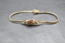 A 9ct gold bracelet having a central panel with three rubies in an open swirl mount on a fixed chain