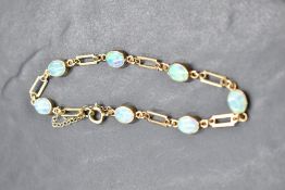 A 9ct gold bracelet having seven collared opals with open link connectors and a safety chain, approx