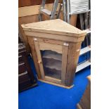 A stripped pine corner wall cupboard having glazed door