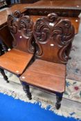 A pair of 19th Century mahogany hall chairs having foliate backs , solid seat and turned legs to