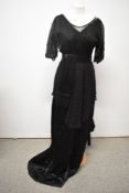 A black Edwardian gown, having sash to waist with tassel detail, lace bodice and overlay to skirt