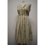 A 1950s medium weight floral cotton day dress having pleated skirt, button front and side press stud