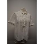 A white 1950s blouse having machine embroidered floral decoration, shaped collar, buttons to front