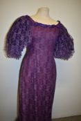 A purple lace evening dress, having stiffened puff sleeves, scoop neckline, train to back of skirt