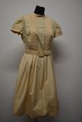 A light beige cotton day dress, having bow to yolk, pin tucks to bodice, plated skirt, self