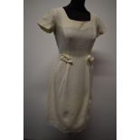 A late 1950s cream textured wiggle dress (wool blend or similar) having scoop neckline bows to hip