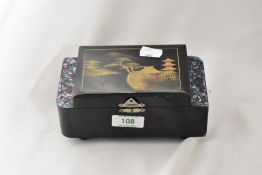 A mid century lacquered musical jewellery box, having inlaid paua shell detail and Japanese scene to