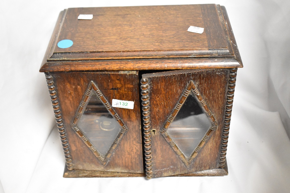 An early 20th century oak smokers cabinet, having two doors with diamond shaped glass and beaded