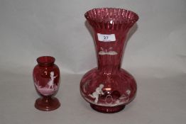 Two Mary Gregory style cranberry glass vases, the largest having a flared and crimped rim, measuring