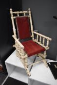 A painted Victorian American child's rocking chair, having spindled supports and a red cloth back