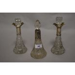 Three Edwardian cut glass lidded scent bottles, with silver and white metal collars, the largest