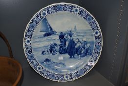 A 20th century large Delft blue charger, having scene of women and children on shore, with sailing