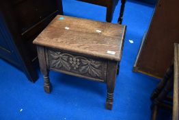 An early 20th Century oak sewing stool having lift lid with vine decoration to front panel